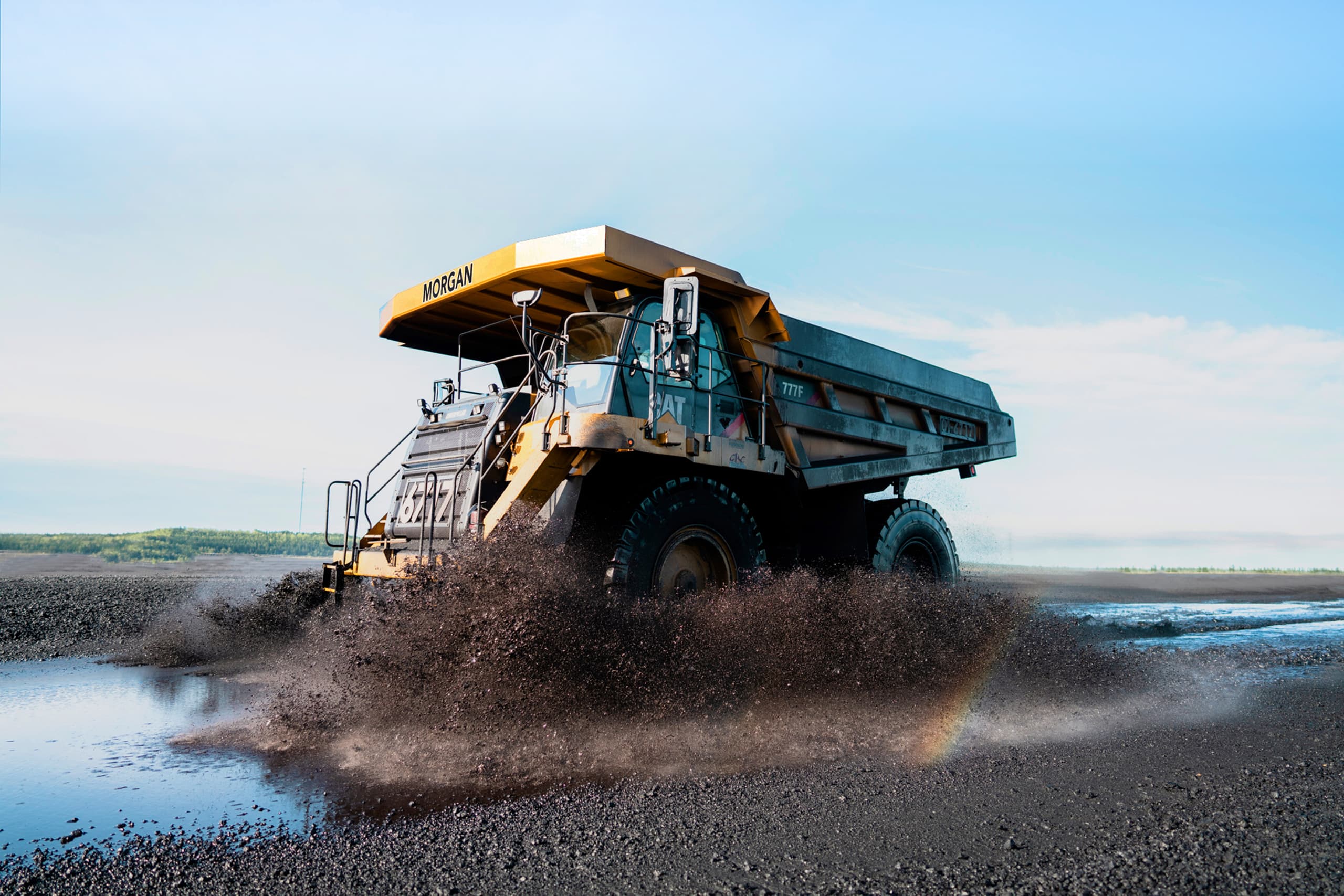 A yellow dump truck driving through water on a dirt road.