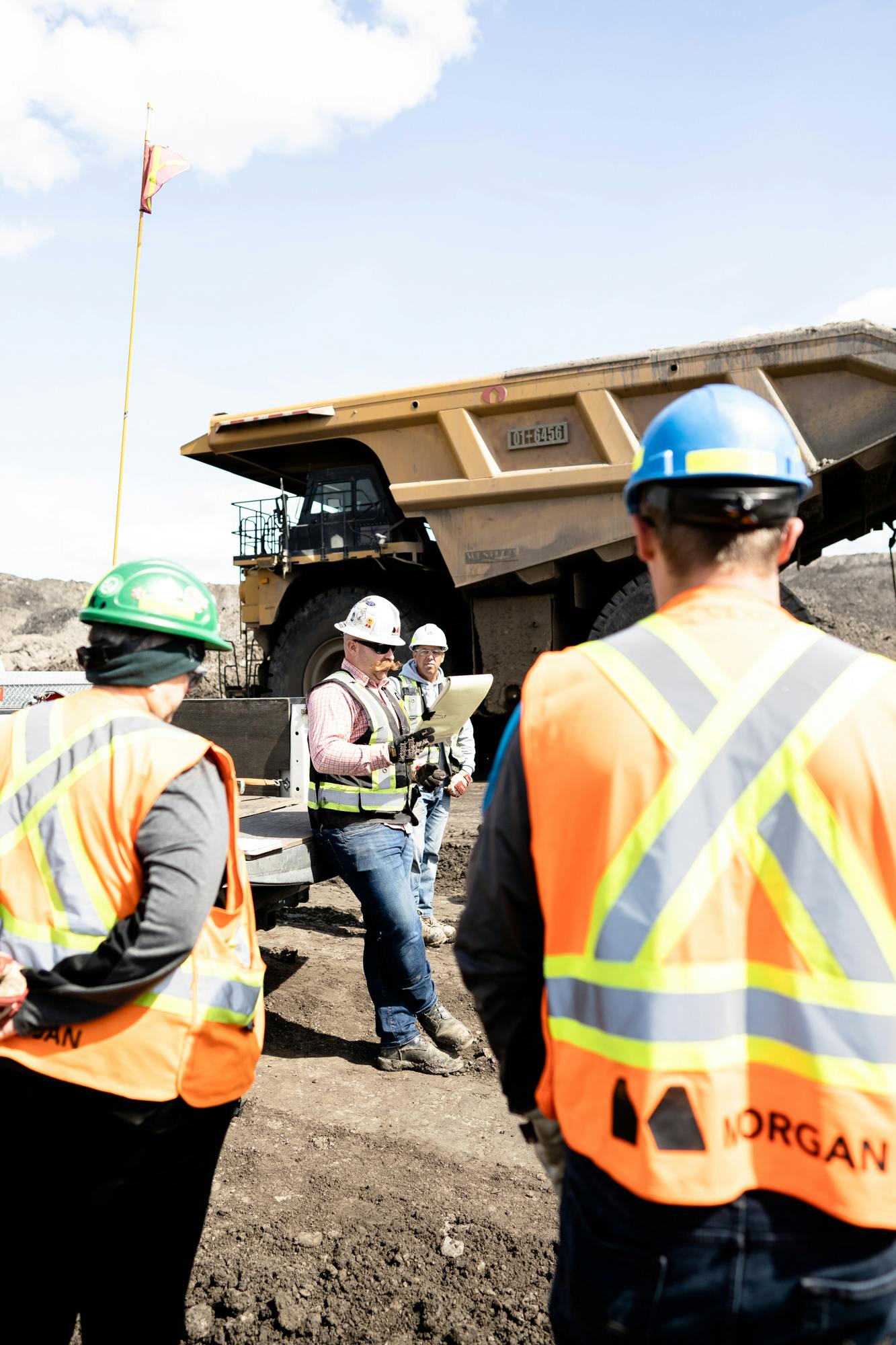 Four construction workers standing near a yellow dump truck.