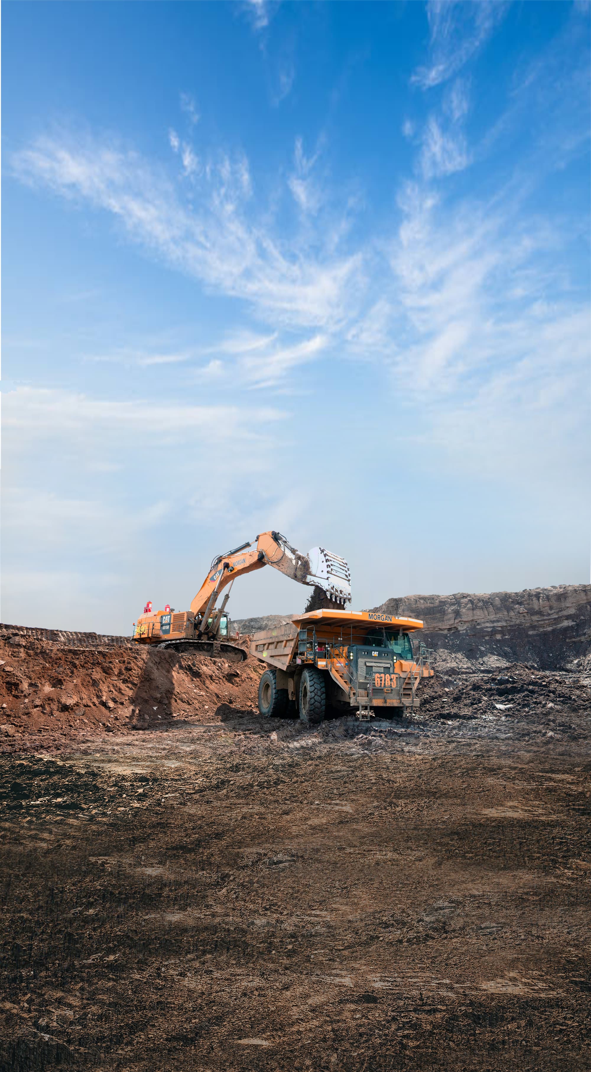 A distant photo of an orange excavator unloading dirt into an orange dump truck.